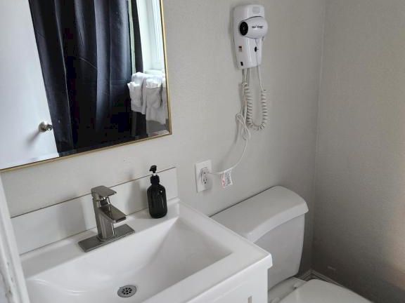 A compact bathroom with a white sink vanity, mirror, towel, wall-mounted hairdryer, and a toilet next to a small counter top space.