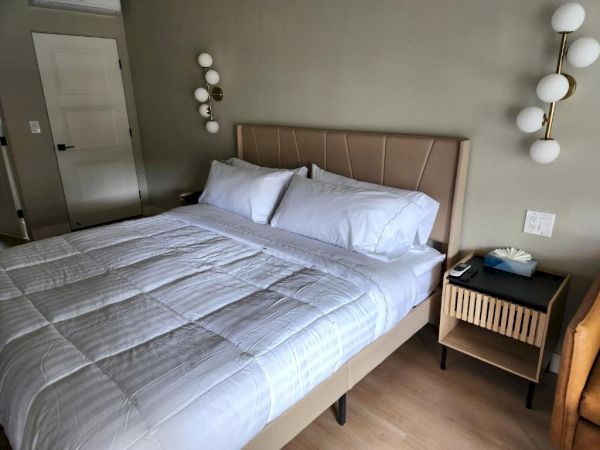 A neatly made hotel-style bed with white bedding, a beige upholstered headboard, nightstands, and modern circular wall lamps on either side.