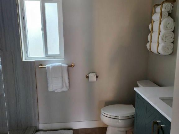 Small bathroom with a glass shower, white toilet, gray vanity, wall towel rack, and a window. Clean and bright.