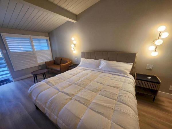 Cozy hotel room with a large bed, soft lighting, a sitting area by the window, and modern bedside tables and lamps.