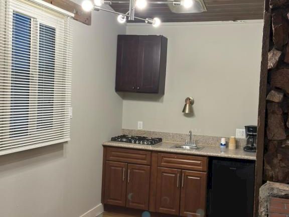 A small kitchen with wooden cabinets, a window with blinds, a gas stove, sink, pendant lights, and a wood-paneled ceiling, compact and cozy.