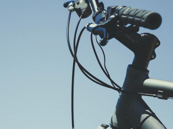 A close-up of a bicycle's handlebar and front fork, with cables, grips, and a mounted light against a clear blue sky.