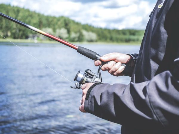 A person is fishing by a lake, holding a spinning reel and rod, ready to cast or reel in.