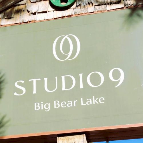 Sign reads &ldquo;STUDIO 9&rdquo; with a logo, and &ldquo;Big Bear Lake&rdquo; on a green sign. It&rsquo;s an outdoor wooden sign against a blue sky.
