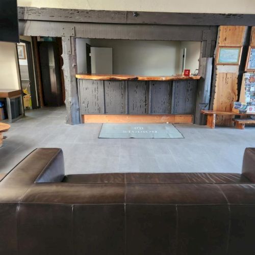 A cozy, rustic lobby with a wooden reception desk, dark leather sofas, and simple benches, giving a cabin-like vibe throughout the space.
