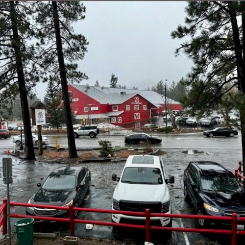 A flooded parking lot near a red building, cars partially submerged, rain-soaked scene with trees and overcast sky.