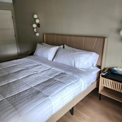 A neatly made bed with white linens, a padded headboard, bedside table, and modern wall light fixtures in a cozy hotel room.